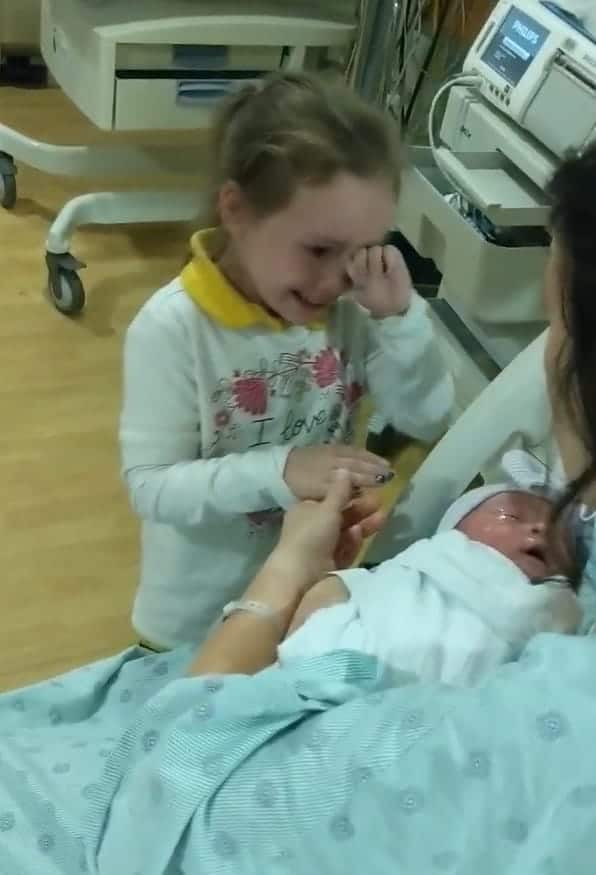 Una bambina non trattiene le lacrime di gioia quando vede la sorellina appena nata.