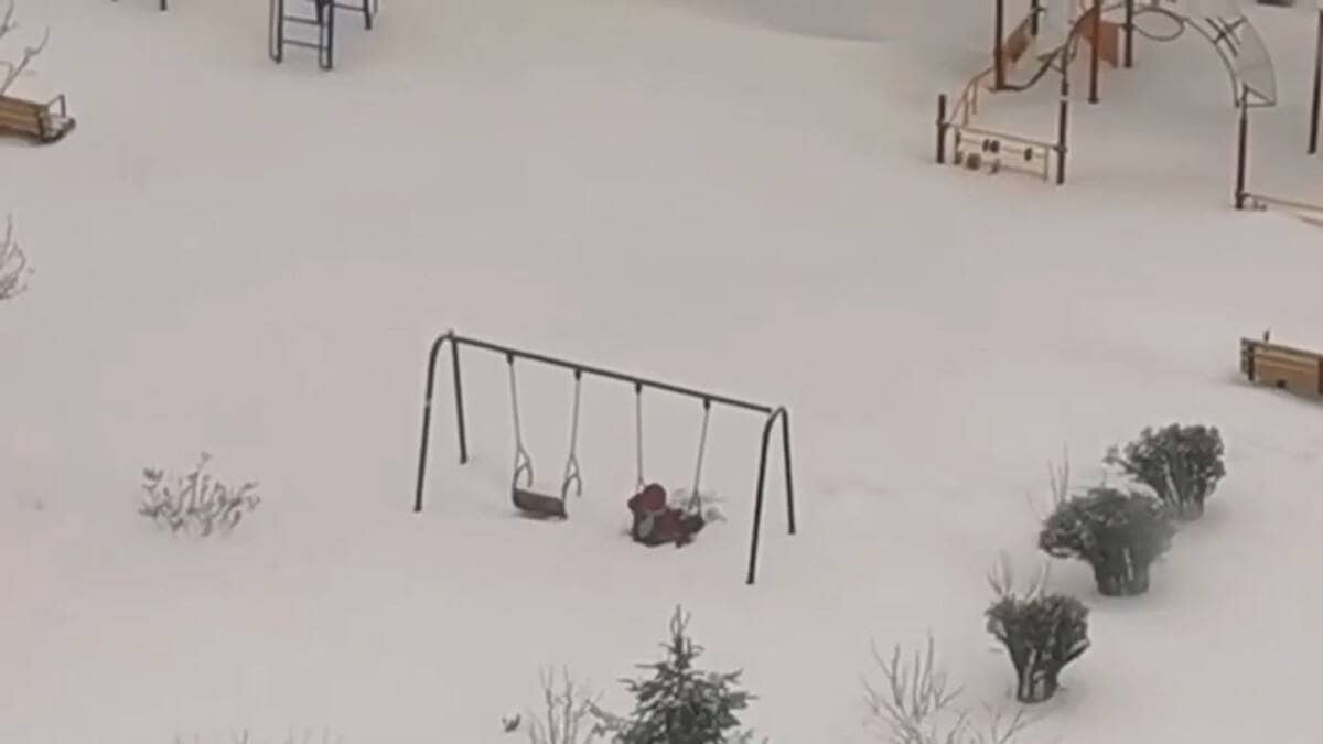 bambino cerca di dondolarsi nel parco giochi innevato